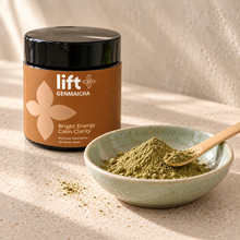 Lift Genmaicha black jar with a brown label beside genmaicha powder in a pale ceramic dish with a bamboo scoop.
