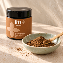 Lift Hojicha black jar with a brown label beside roasted tea powder in a pale ceramic dish with a bamboo scoop.
