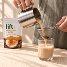 Milky chai being poured through a fine mesh strainer into a glass, with a Lift Fresh Chai pouch in the background.