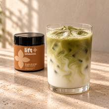 Iced genmaicha latte serving suggestion in a clear glass with a Lift Genmaicha black jar on a warm stone counter.