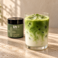 Iced matcha latte serving suggestion in a clear glass, with a Lift Matcha black jar on a warm stone counter.