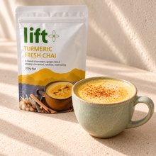 Golden turmeric chai latte serving suggestion in a pale ceramic cup beside a Lift Turmeric Fresh Chai pouch.
